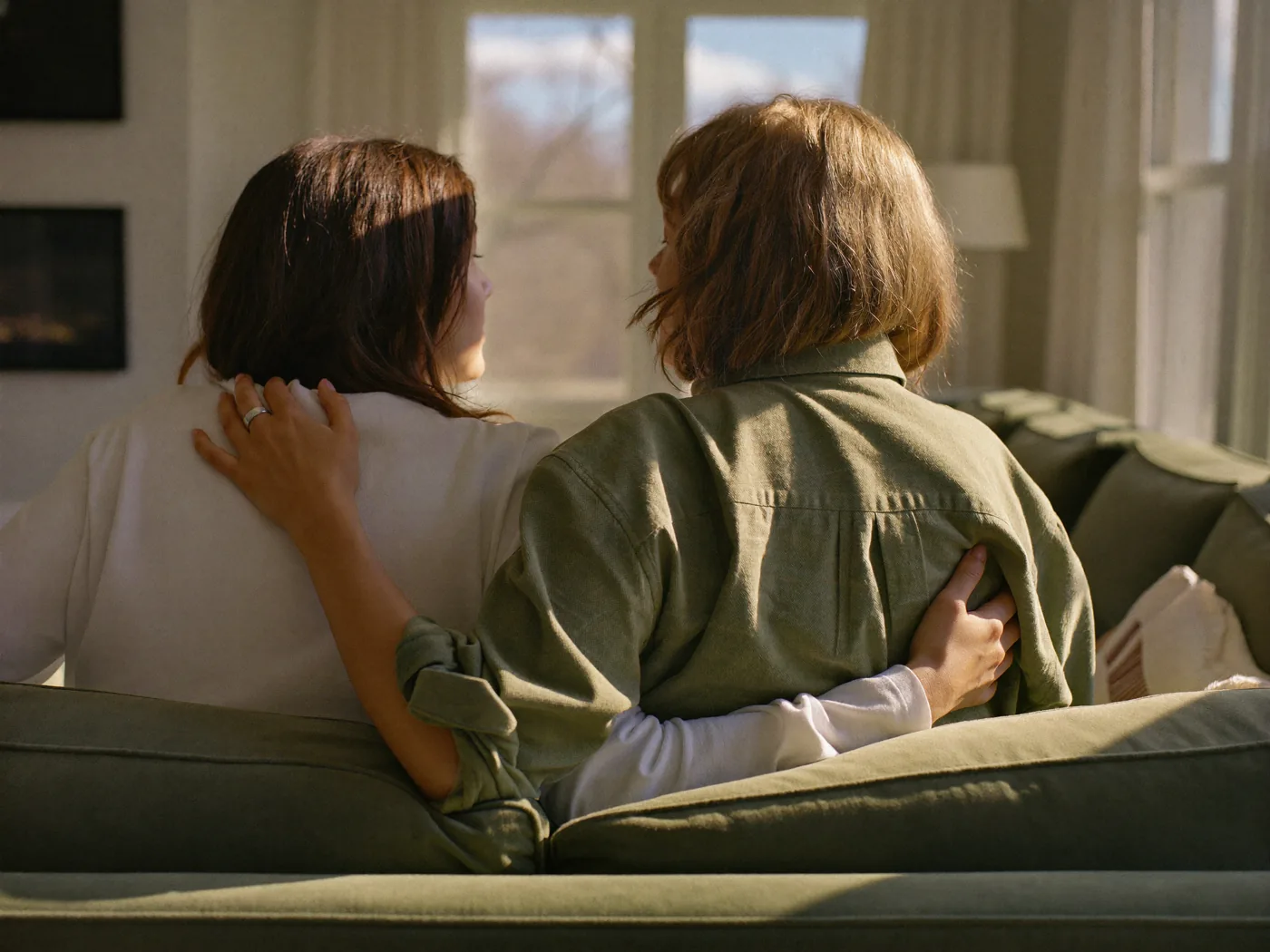 Two women sitting together, one with an arm around the other, seen from behind