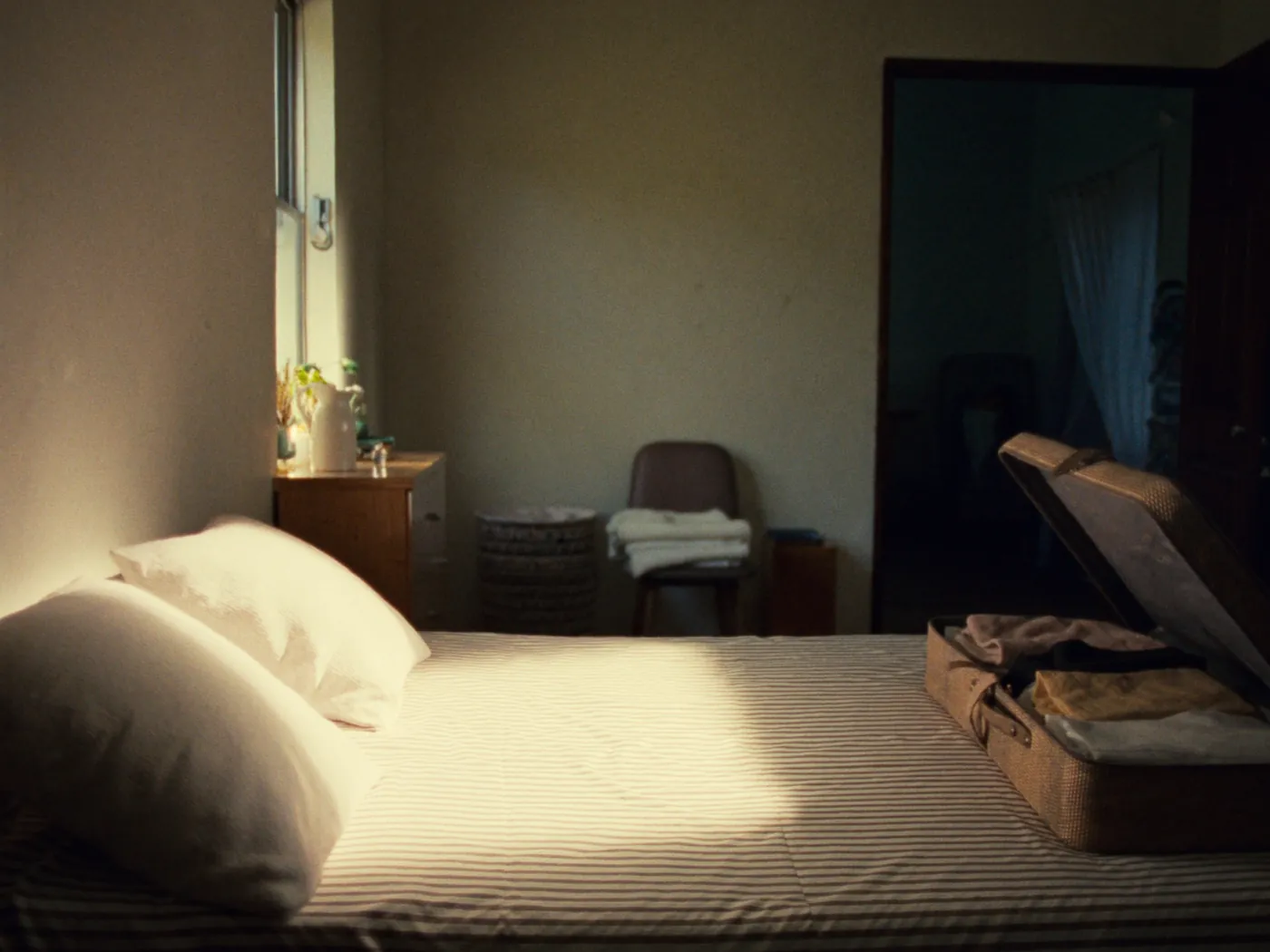 An open suitcase on a made bed in a sunlit room