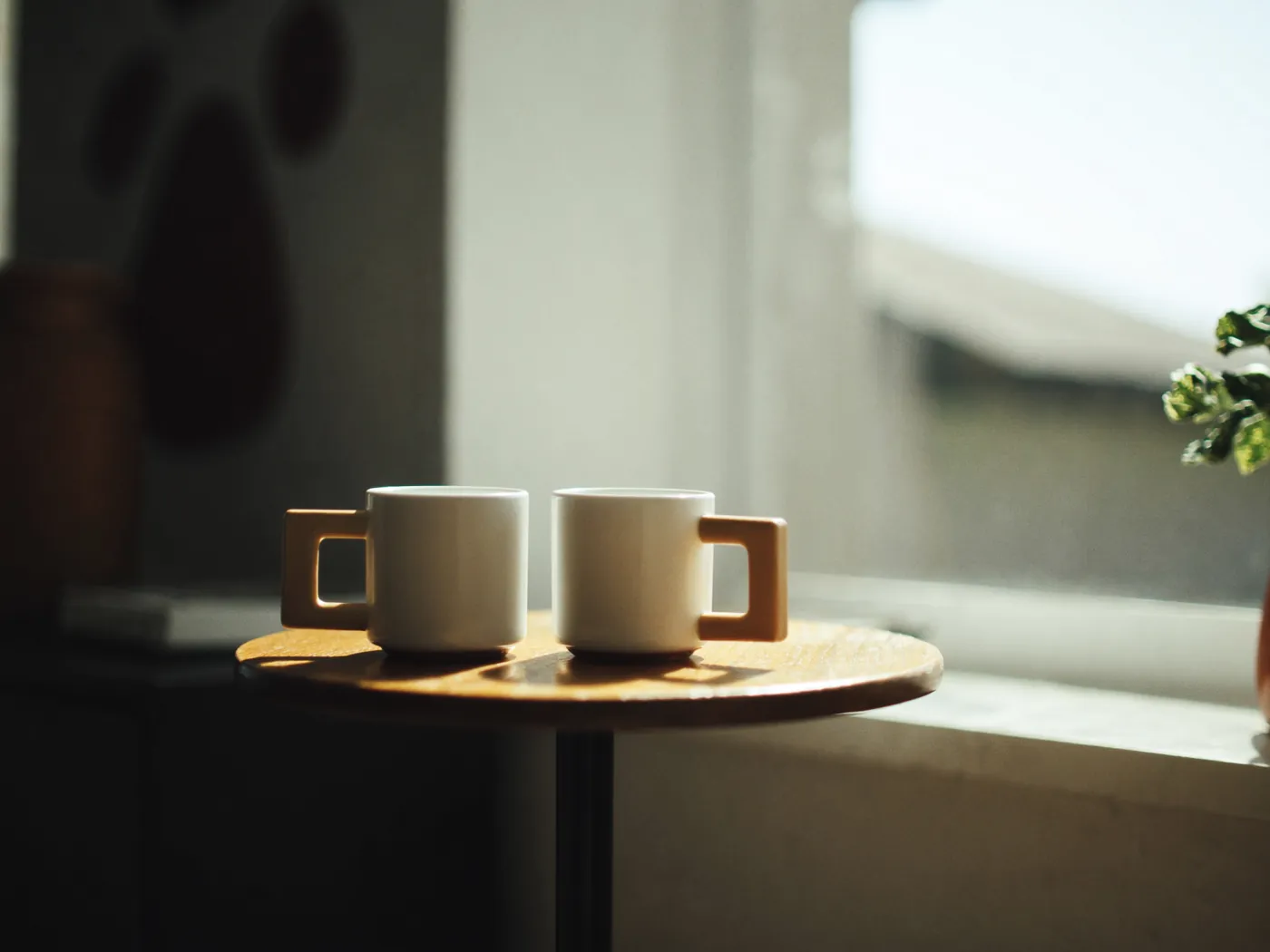 Two cups of coffee on a small table by a bright window